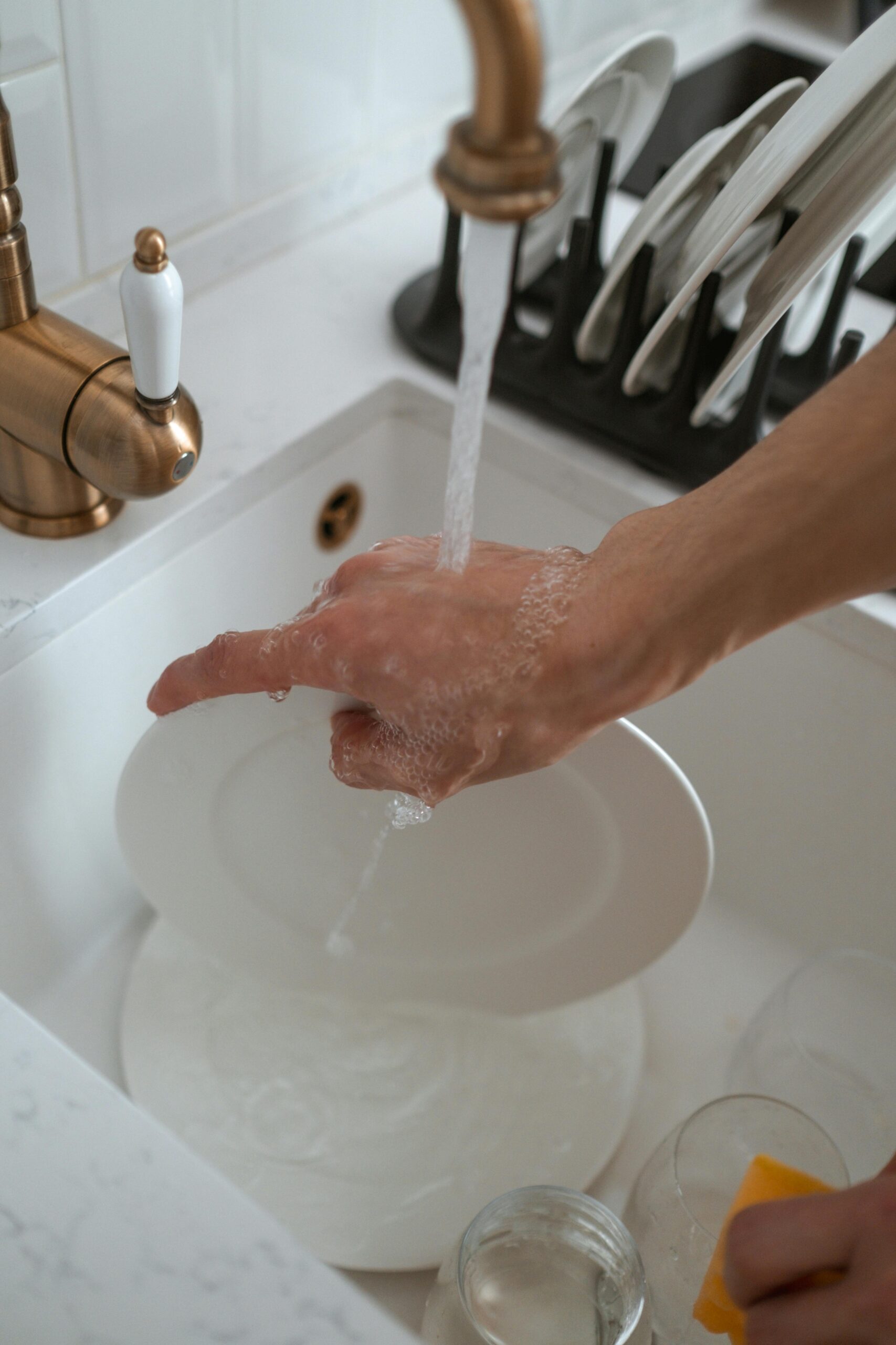 Close-up of hand washing dishes in a kitchen sink with water flowing from faucet.